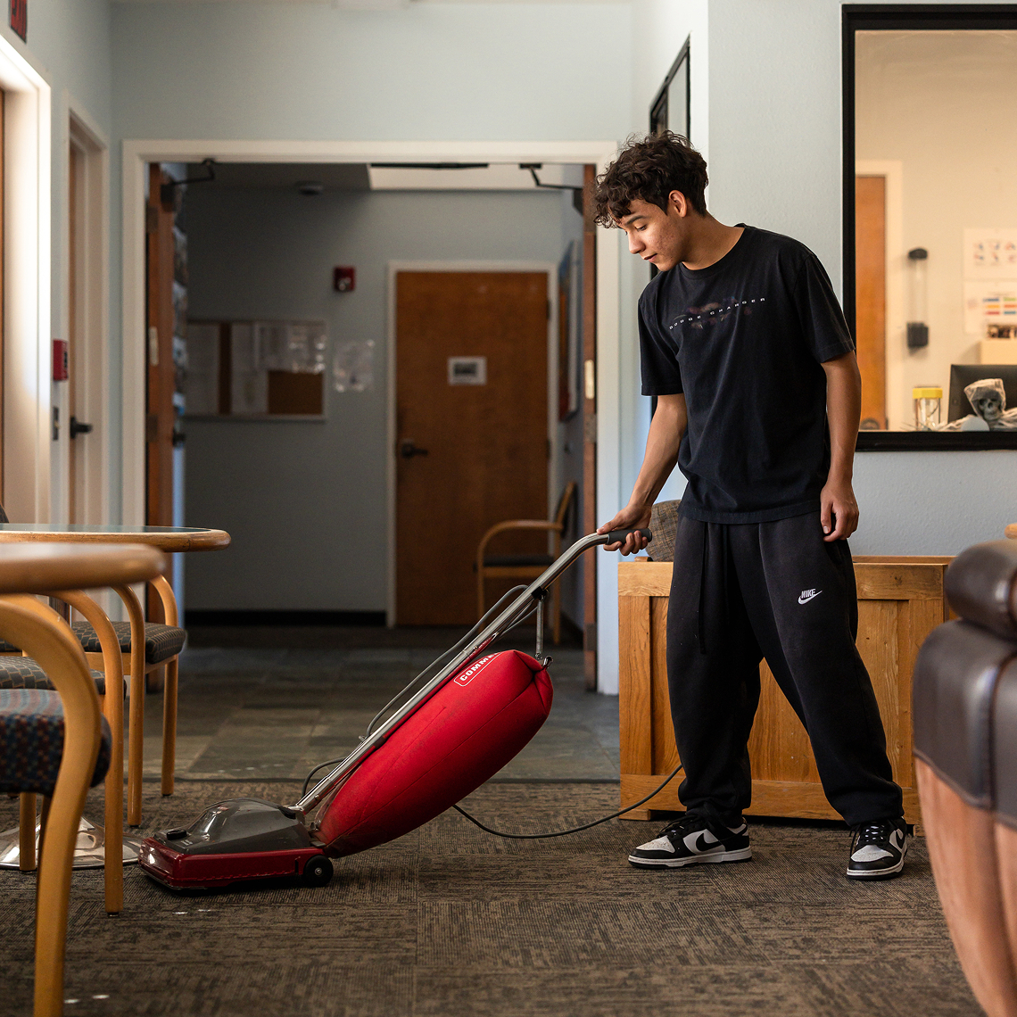 Student vacuuming a carpet in a common area.