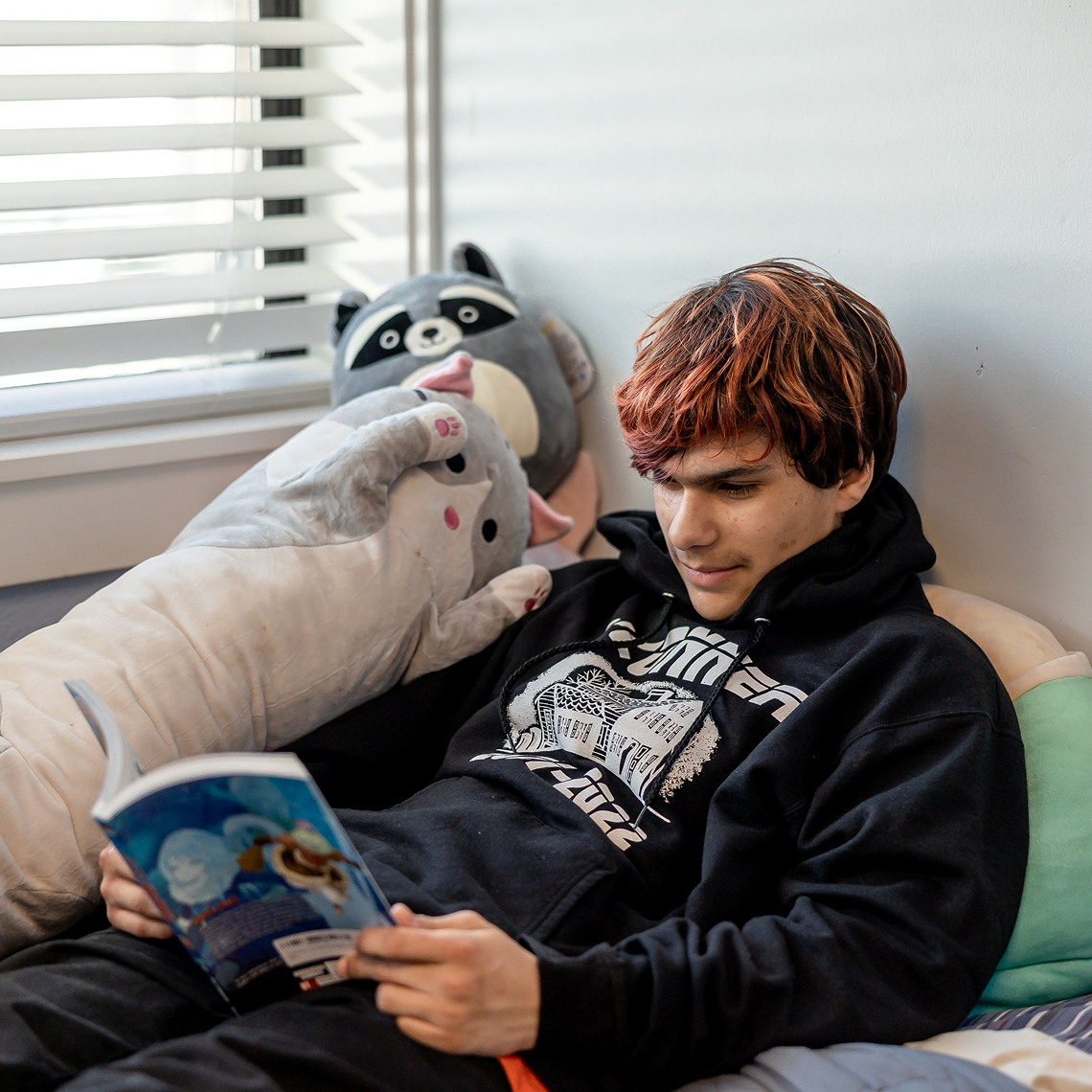 Student reading a book while sitting with a stuffed animal.