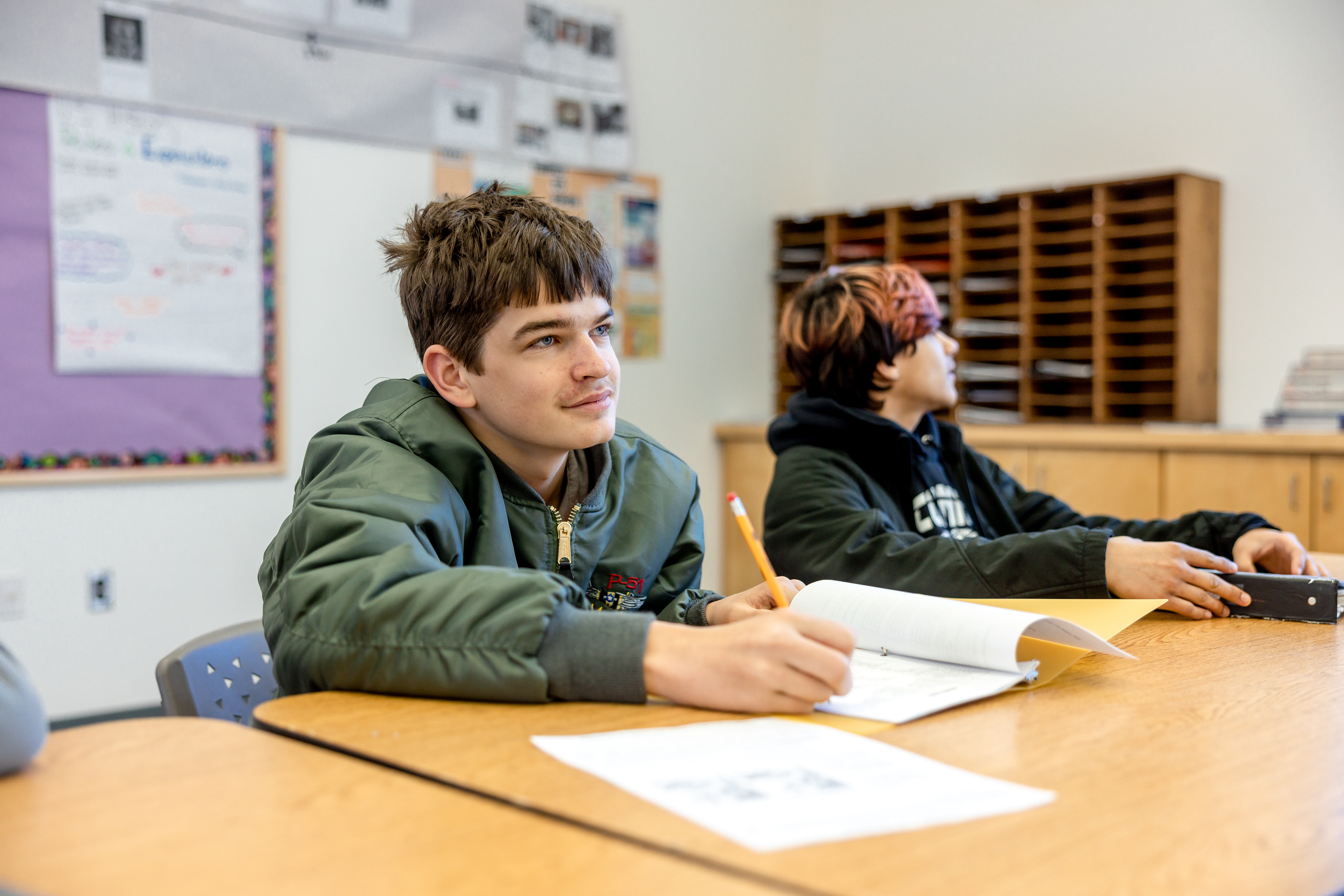 Student sitting in classroom writing at desk.