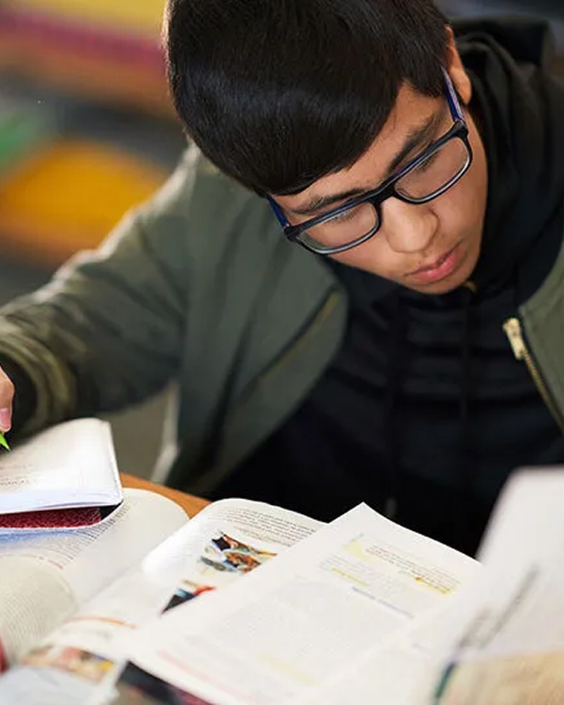 Student studying and writing notes in a textbook.