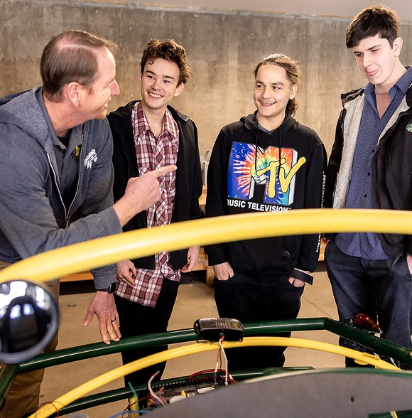 Faculty member instructing students around a mechanical project.