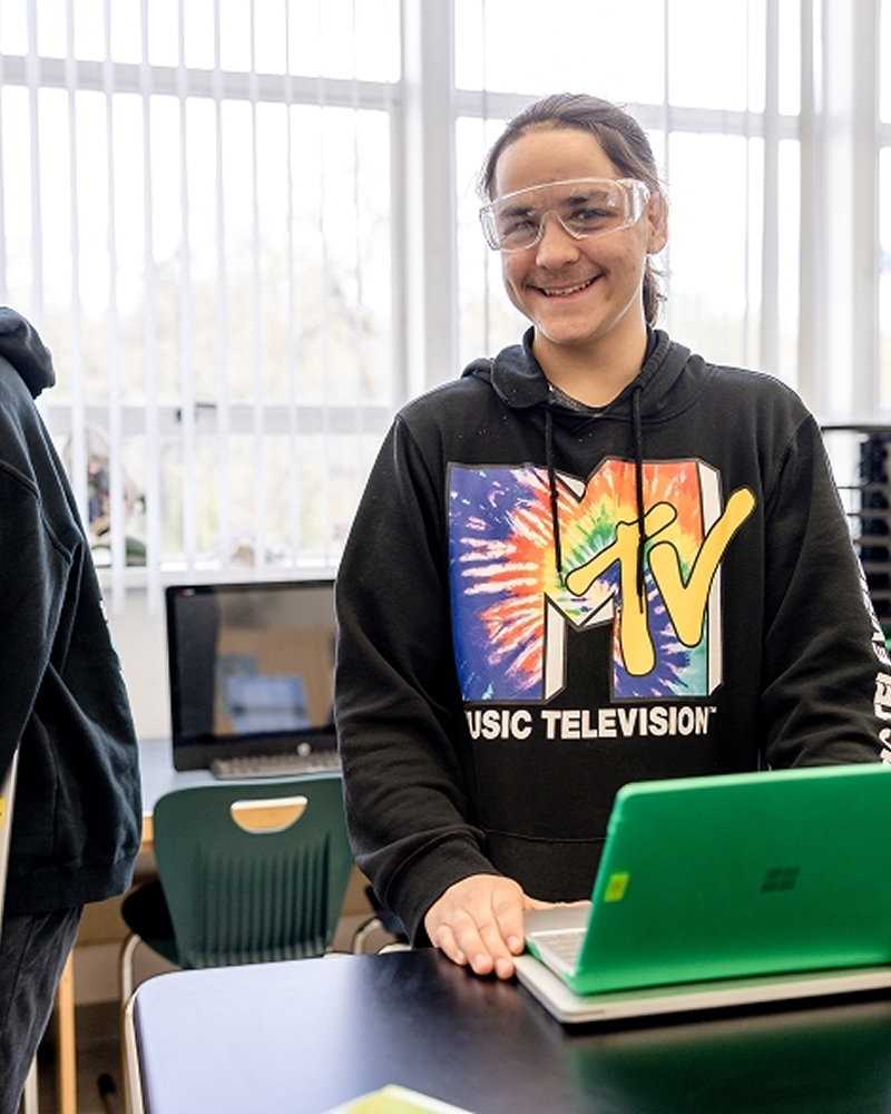 Student smiling with laptop in classroom.