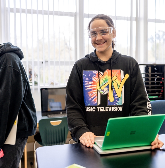 Student smiling with laptop in classroom.