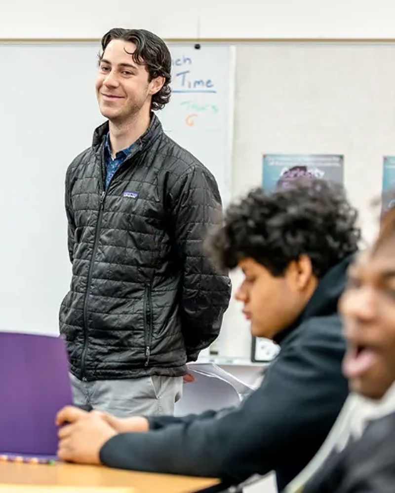 Teacher standing at the front of the classroom with students listening.