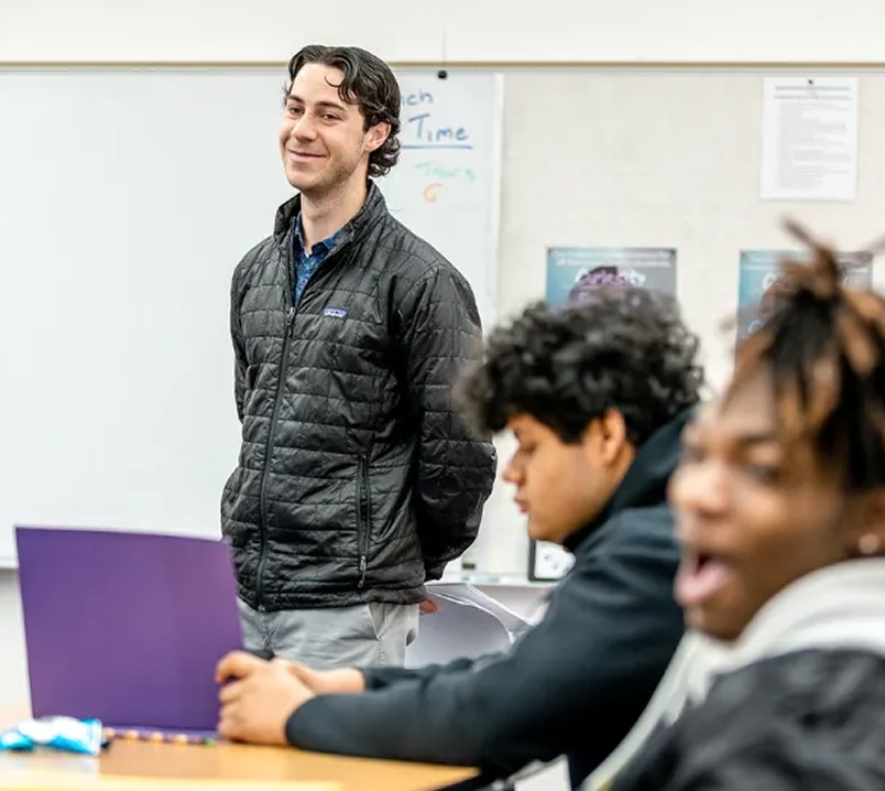 Teacher standing at the front of the classroom with students listening.