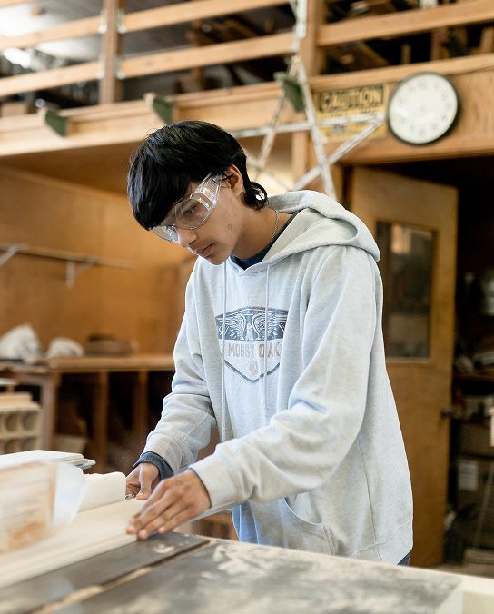 Student wearing safety goggles using a woodworking machine in class