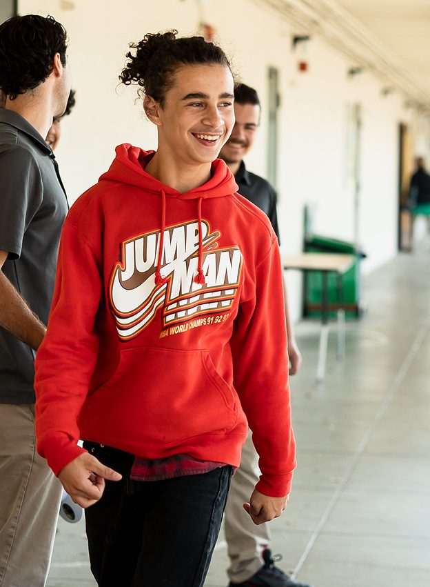 Smiling student in a red hoodie walking down the hallway at Hanna Academy