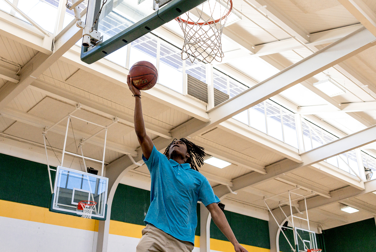 Student shooting a basketball during gym activity.