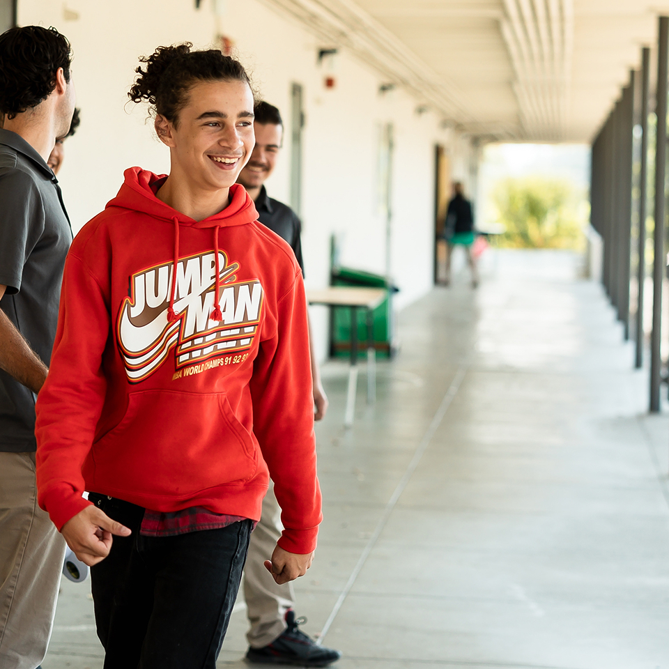 Student in red hoodie walking down the school hallway.